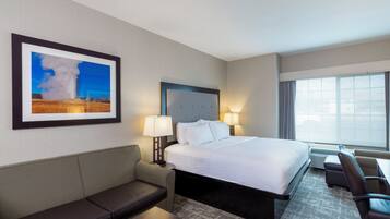A hotel room with a bed, a sofa, a desk, and a large window.