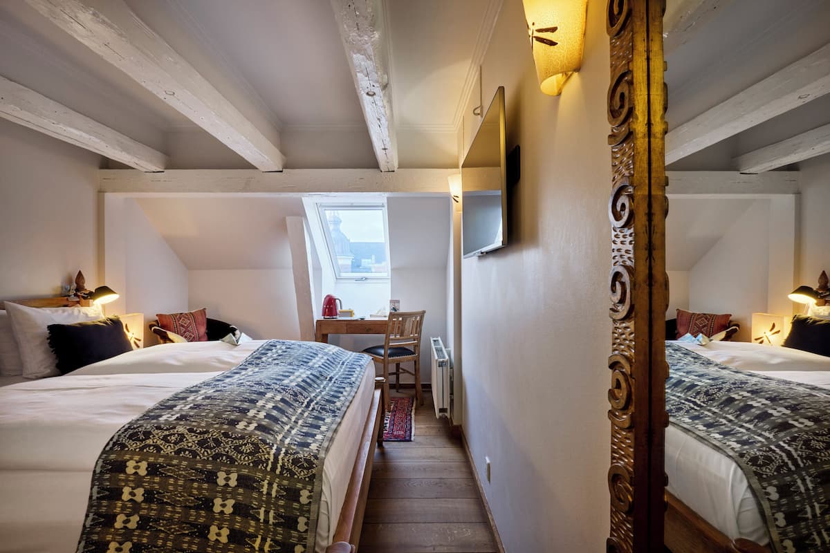 A bedroom with two beds, a desk, a chair, a radiator, and a TV mounted on the wall.
