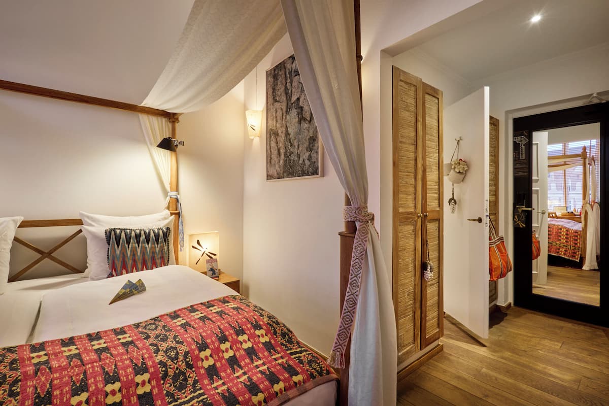 A bedroom with a bed, a nightstand, a bedside lamp, a canopy bed, a wardrobe, and a mirror.