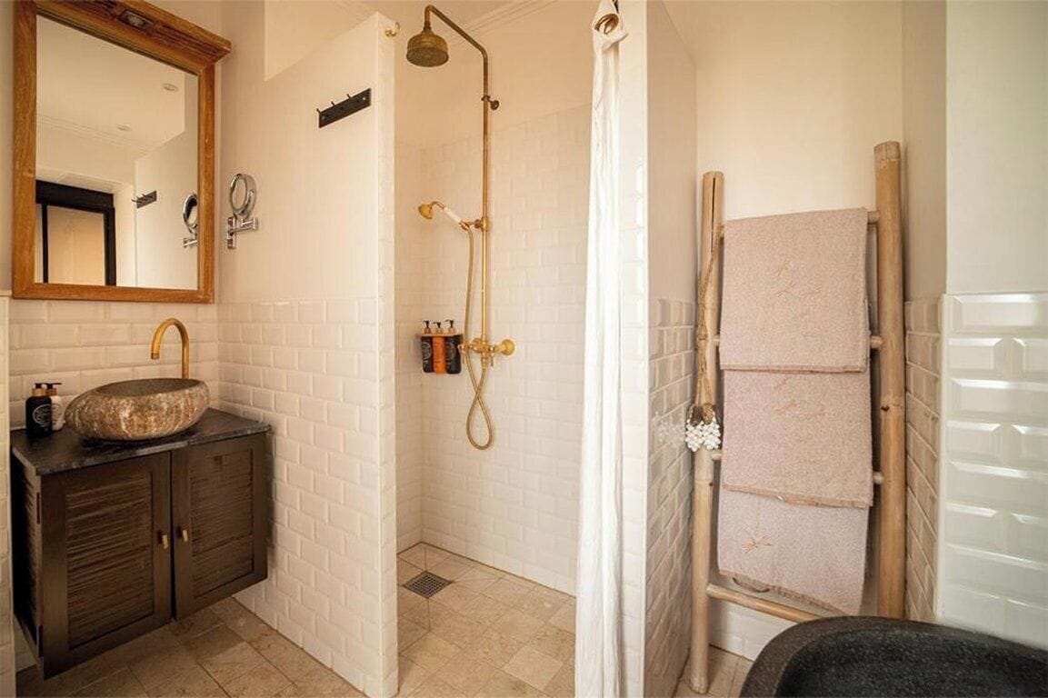A bathroom with a stone sink, a mirror, a shower with a wooden door, and a towel rack.