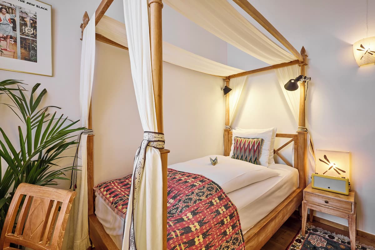 A four-poster bed with a canopy, a bedside table with a lamp, and a wall-mounted clock.