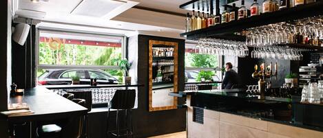 Un área de bar con mostrador, taburetes y una estantería llena de botellas de licores.