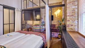 Une chambre moderne avec un grand lit, une cloison en verre, un fauteuil suspendu aux couleurs vives et un mur en briques.