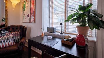 A modern living room with a leather armchair, a desk with a laptop, a potted plant, and a red kettle.