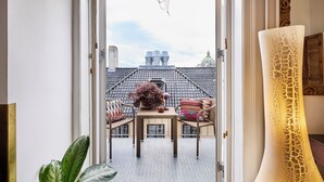 Un balcon donnant sur le toit d’un immeuble, une table avec des chaises et une lampe décorative.