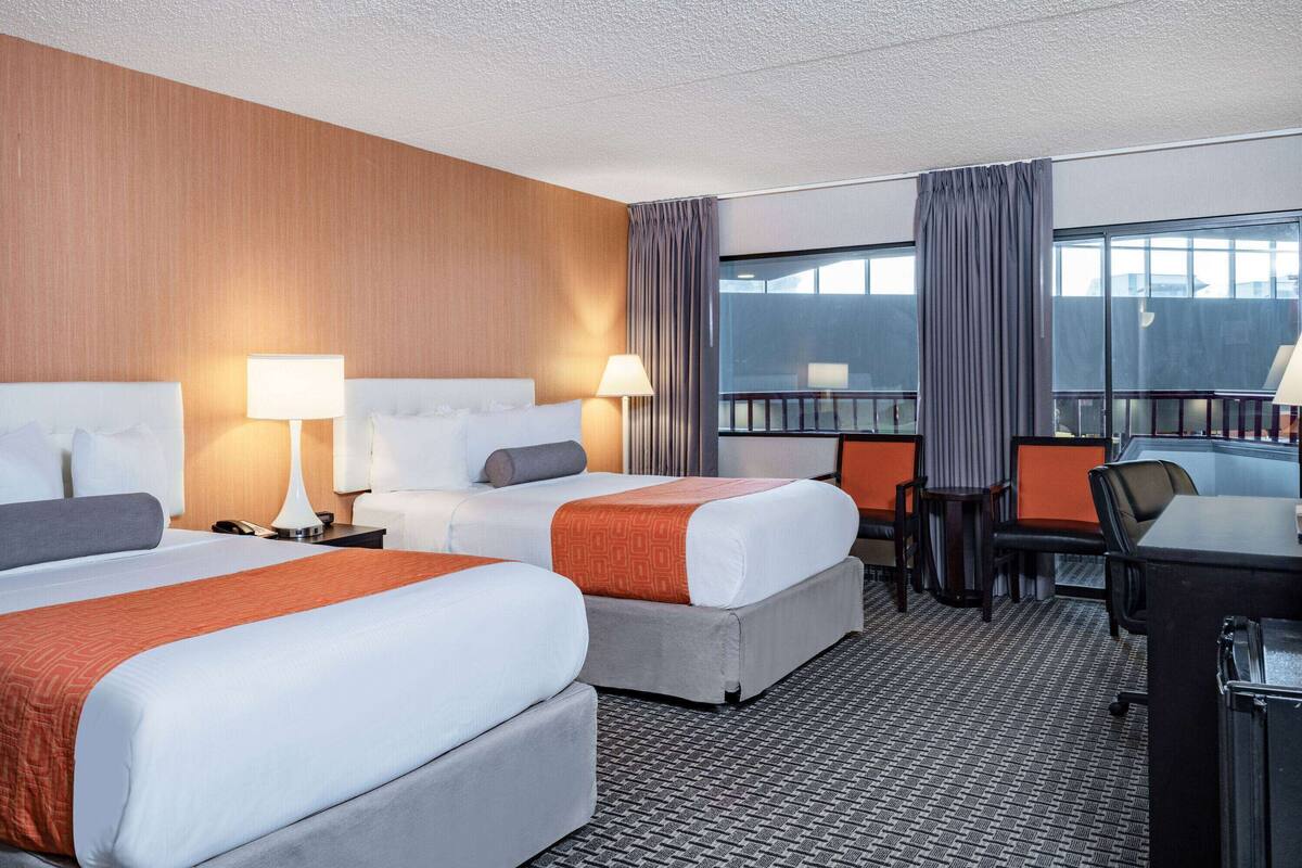 A hotel room with two beds, a desk, and a balcony.
