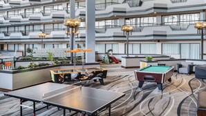 Un espacio recreativo interior de varios niveles con mesas de ping pong, mesas de billar y una zona de juegos para niños.