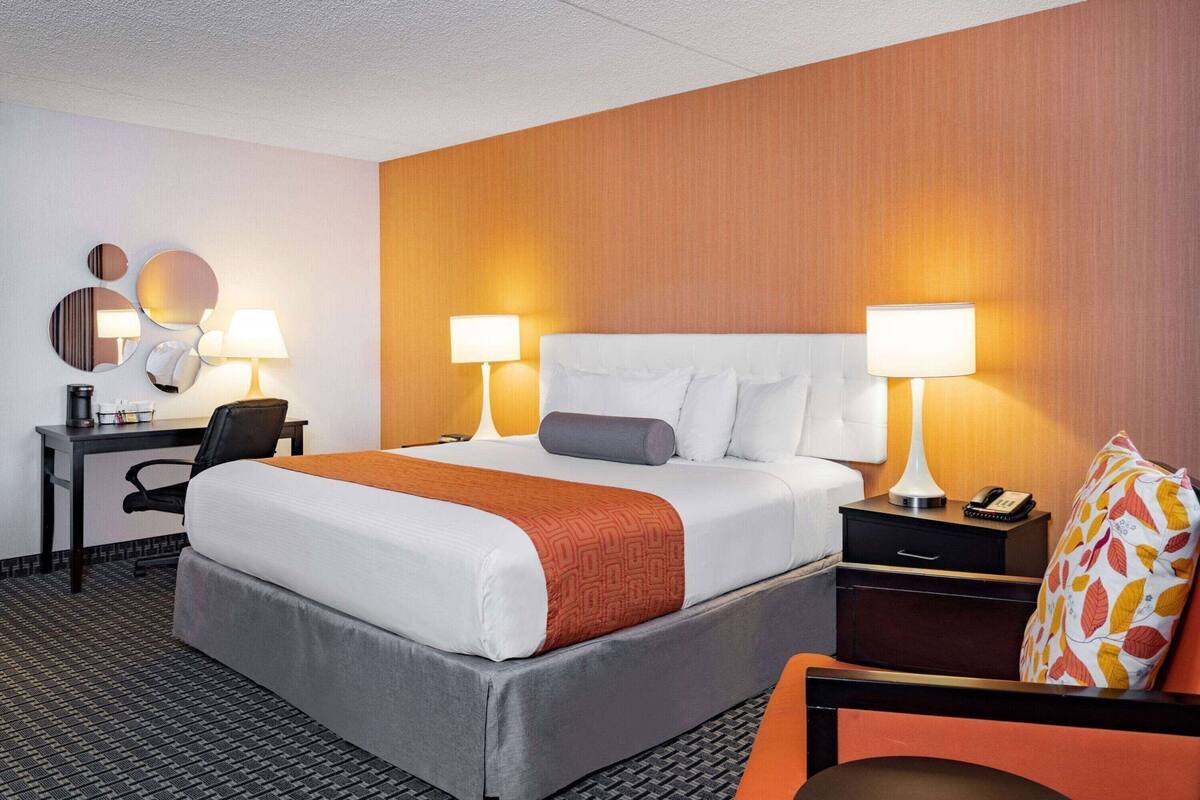 A hotel room with a bed, two bedside tables, a desk, a chair, and a lamp.