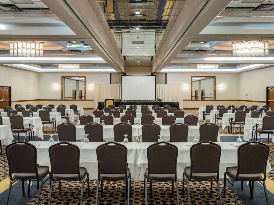 A conference room with rows of tables and chairs, a large screen at the front, and chandeliers on the ceiling.