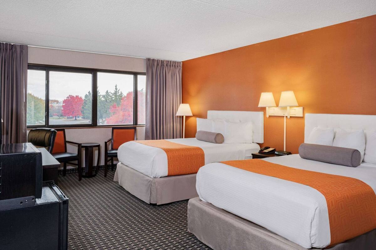 A hotel room with two beds, a desk, a chair, and a TV.