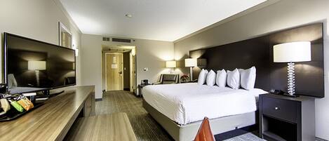 Una habitación de hotel con cama, mesita de noche, lámpara, televisión y escritorio con silla.