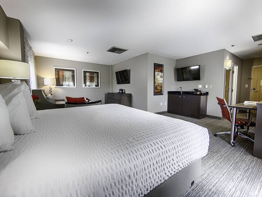 A hotel room with a large bed, a desk with a chair, a television, and a wardrobe.