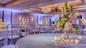 A banquet hall with round tables, chairs, and floral centerpieces.