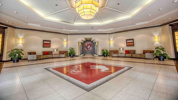 A spacious lobby with a central red carpet, seating areas, and a large chandelier.