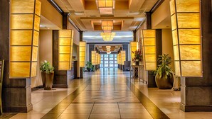 A hotel lobby with a long corridor, large potted plants, and a modern chandelier.
