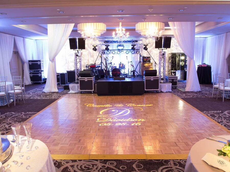 A wedding reception area with a dance floor, stage, and seating arrangements.