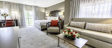 A hotel room with a bed, a sofa, a chair, a desk, and a coffee table.