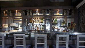 A bar area with a counter, shelves of bottles, and bar stools. - Howard Johnson by Wyndham Niagara Falls (Niagara Falls)