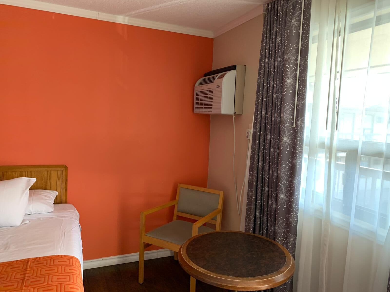 A hotel room with a bed, a chair, a small table, and a window with curtains.