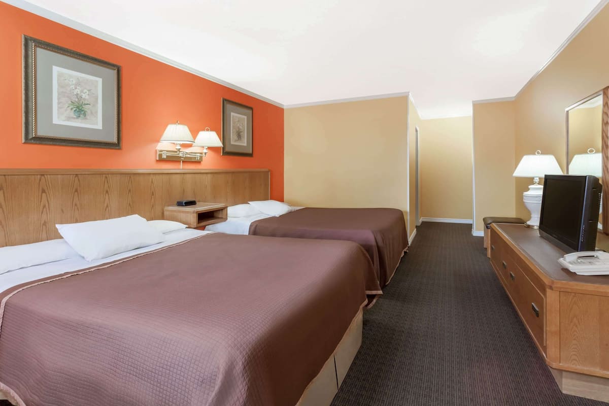 Ein Hotelzimmer mit zwei Betten, einem hölzernen Kopfteil, einem Schreibtisch mit Fernseher und einem Spiegel.