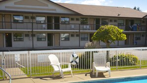 A swimming pool with two white lounge chairs, a fenced area, and a building with multiple windows and balconies in the background. - Howard Johnson by Wyndham Niagara Falls (Niagara Falls)