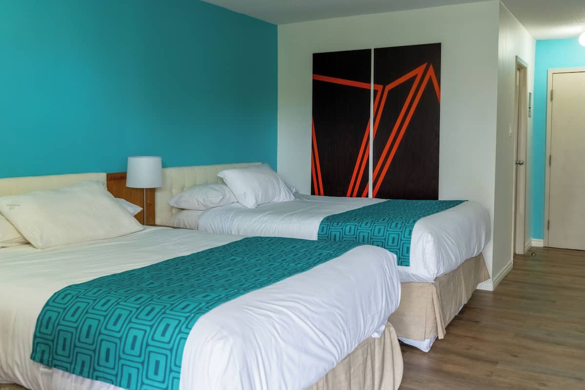 Ein Hotelzimmer mit zwei Betten, einem Nachttisch, einer Lampe und einem großen, abstrakten Kunstwerk an der Wand.