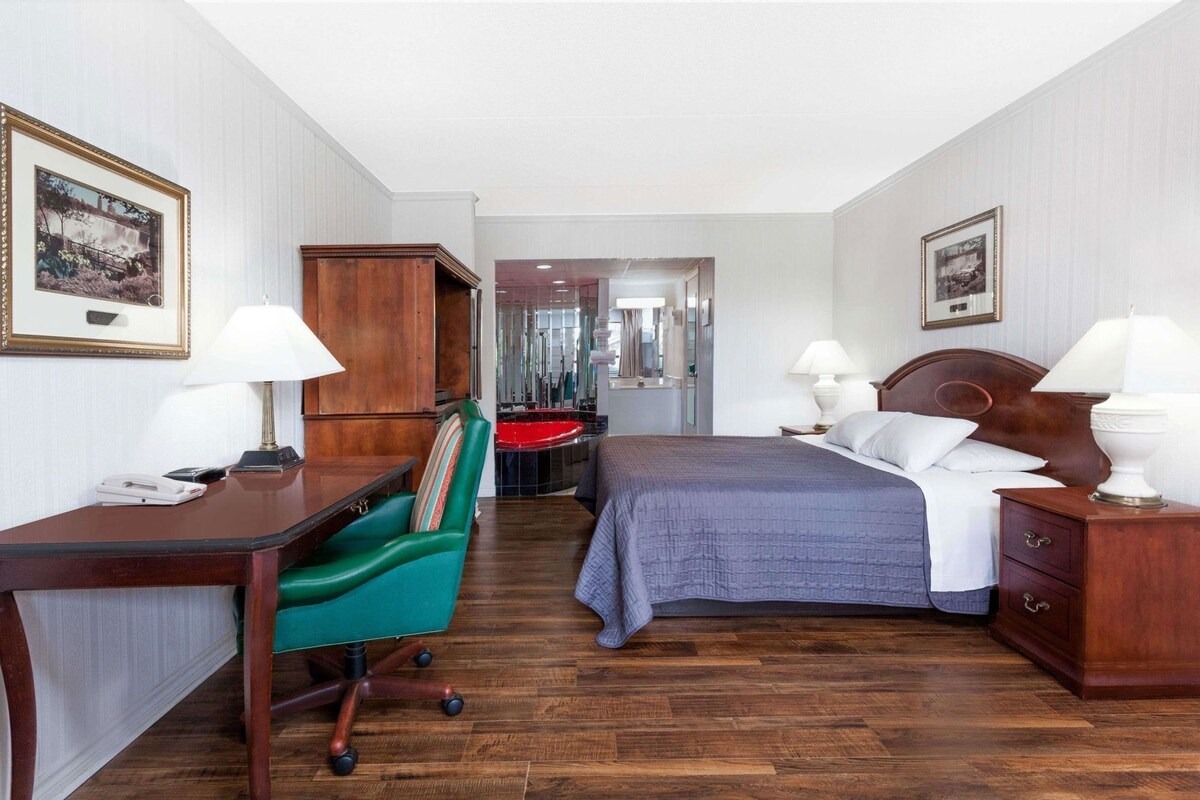 A hotel room with a bed, desk, chair, and a bathroom visible through an open door.