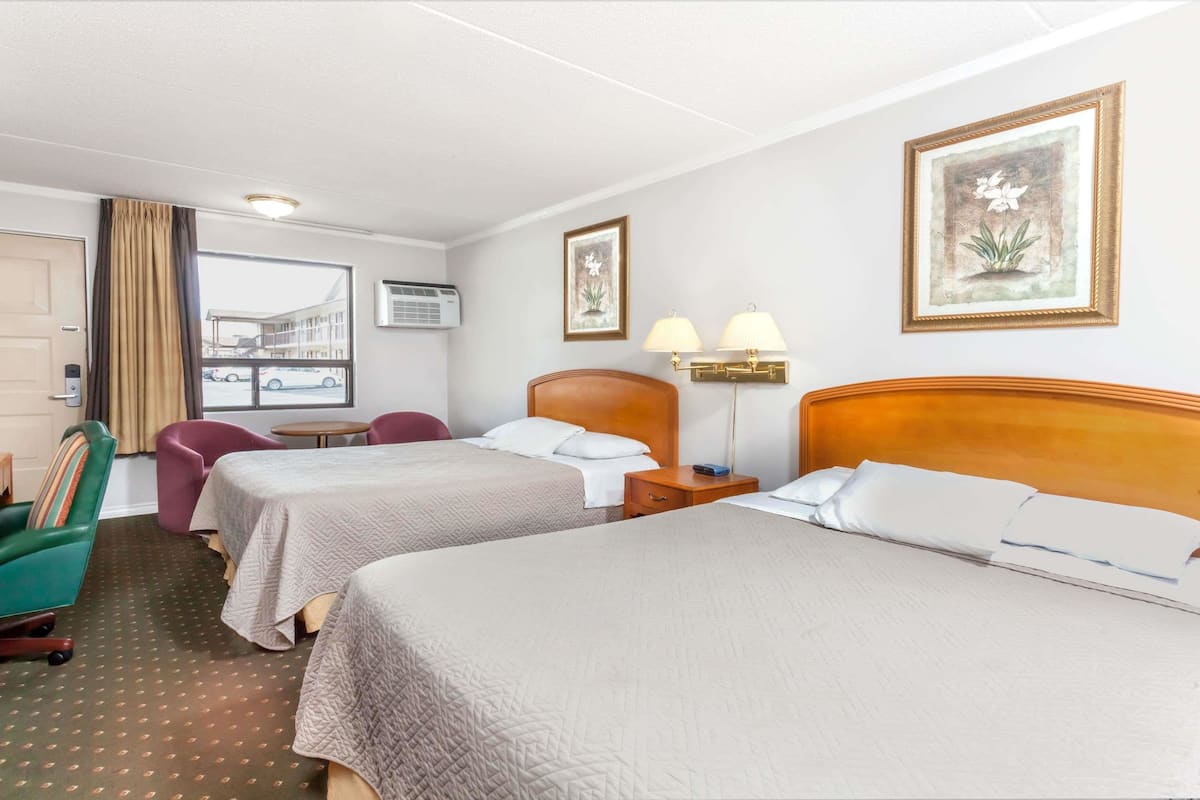 Ein Hotelzimmer mit zwei Betten, einem Schreibtisch, einem Stuhl, einem Fenster und einem gerahmten Bild an der Wand.