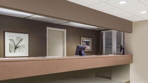 A reception desk with framed artwork, a computer, and a window with blinds. - Howard Johnson by Wyndham Niagara Falls (Niagara Falls)