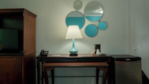 A room with a wooden desk, a teal desk lamp, a telephone, a coffee maker, a refrigerator, and a wall-mounted mirror. - Howard Johnson by Wyndham Niagara Falls (Niagara Falls)