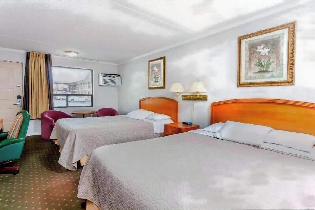 Ein Hotelzimmer mit zwei Betten, einem Fenster mit Blick, einem Sessel, einem Tisch und einer Lampe.