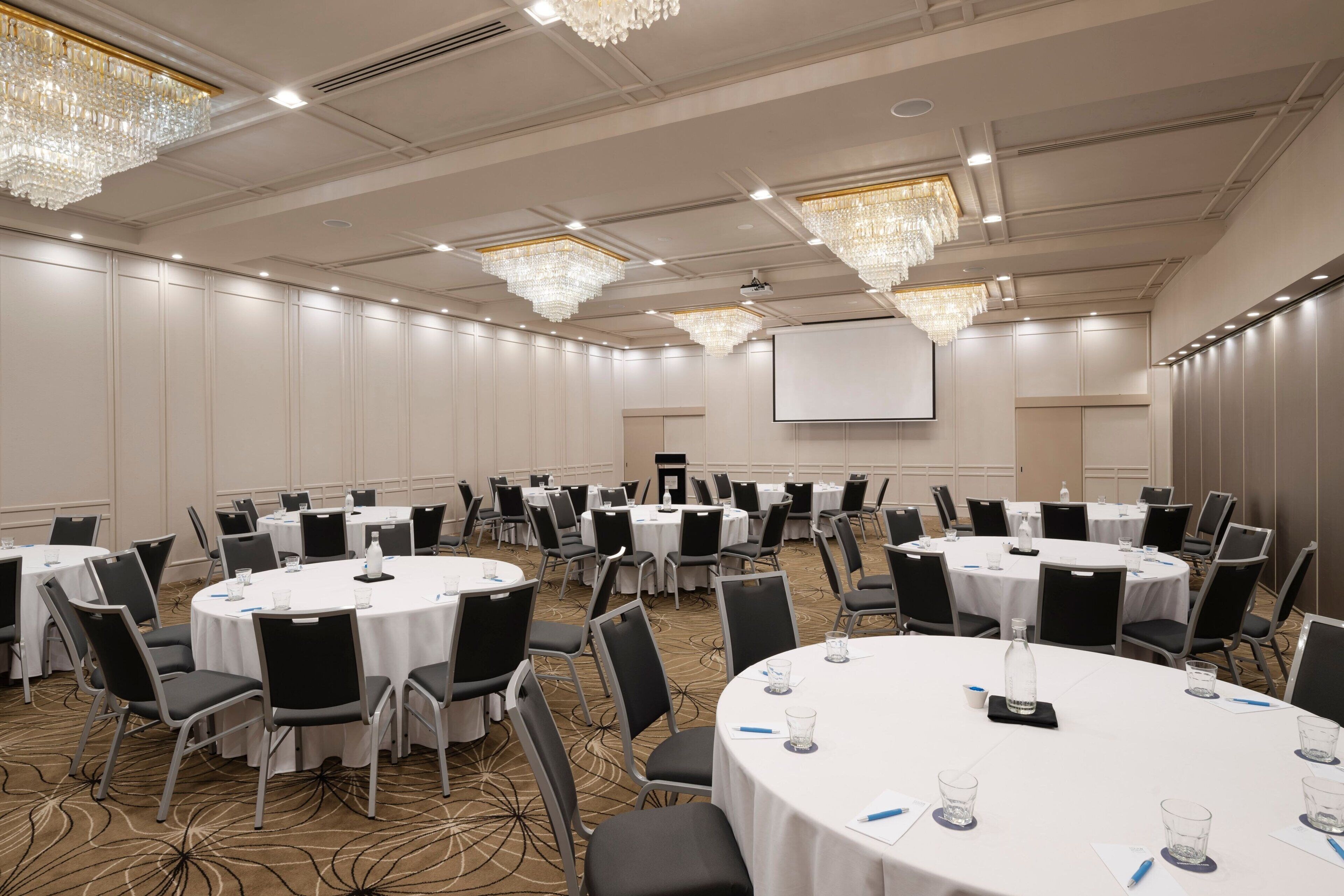 A conference room with round tables, black chairs, and chandeliers.