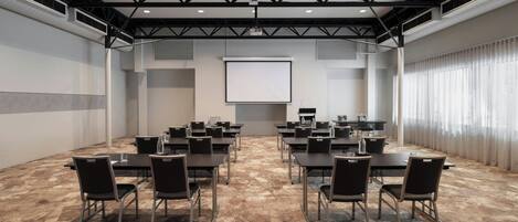 A conference room with a projector screen, multiple tables, and chairs arranged for meetings.