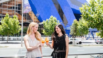 Dos mujeres brindando con bebidas frente a un edificio moderno con fachada de vidrio azul.