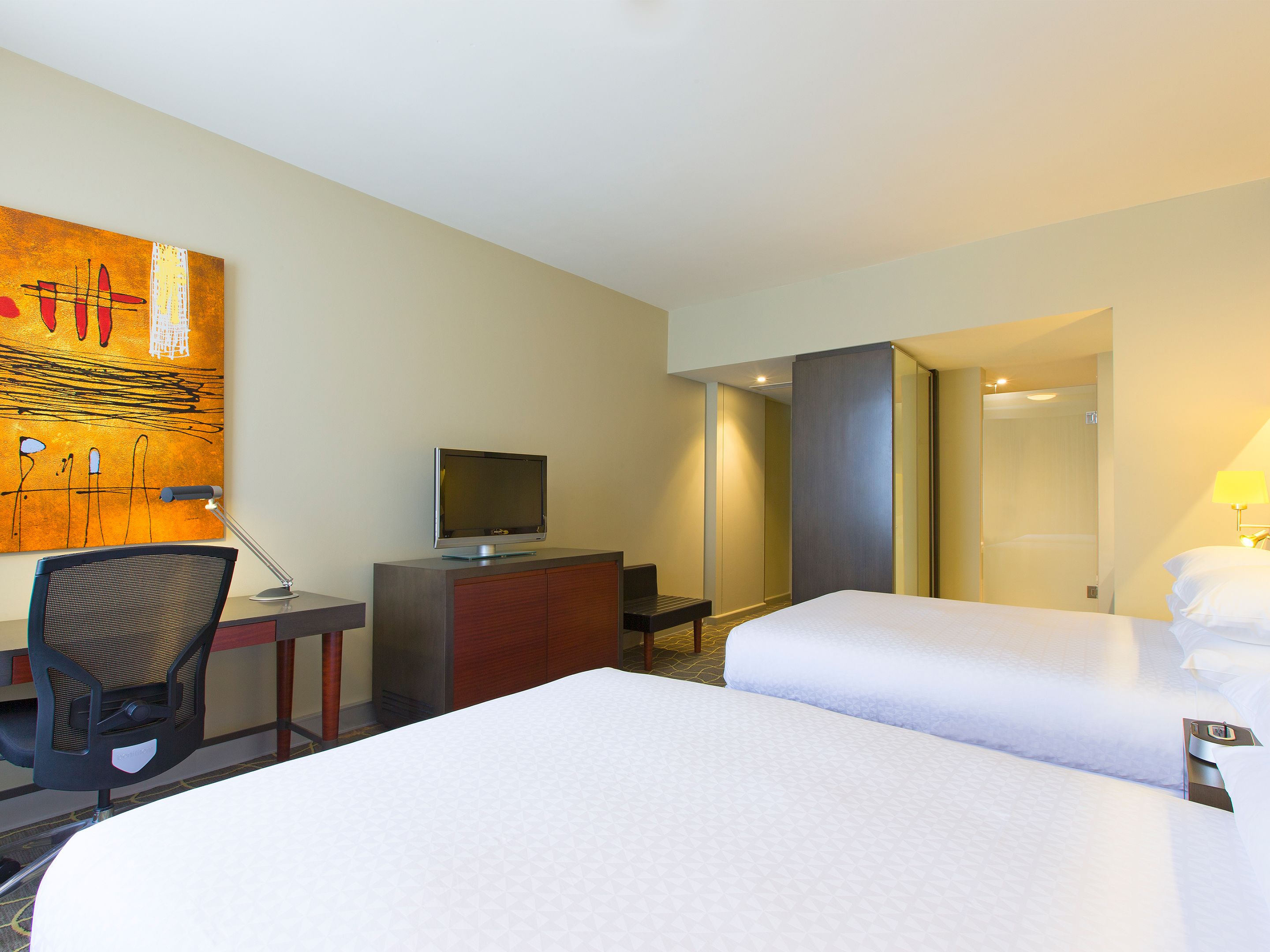 Habitación de hotel con cama, escritorio con computadora, televisión y un cuadro en la pared.