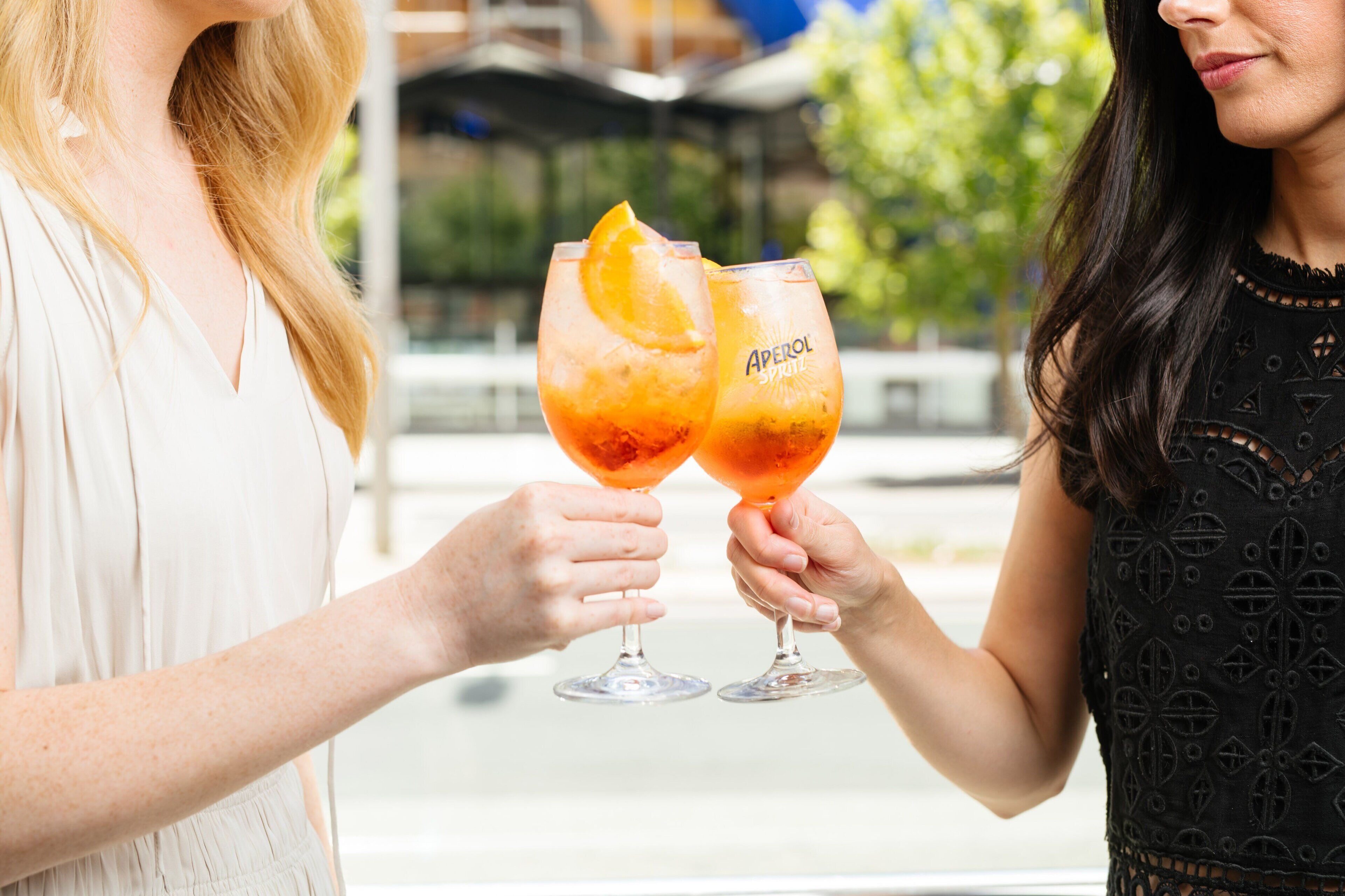 Två personer håller i glas med en rosa drink, garnerad med en apelsinskiva.