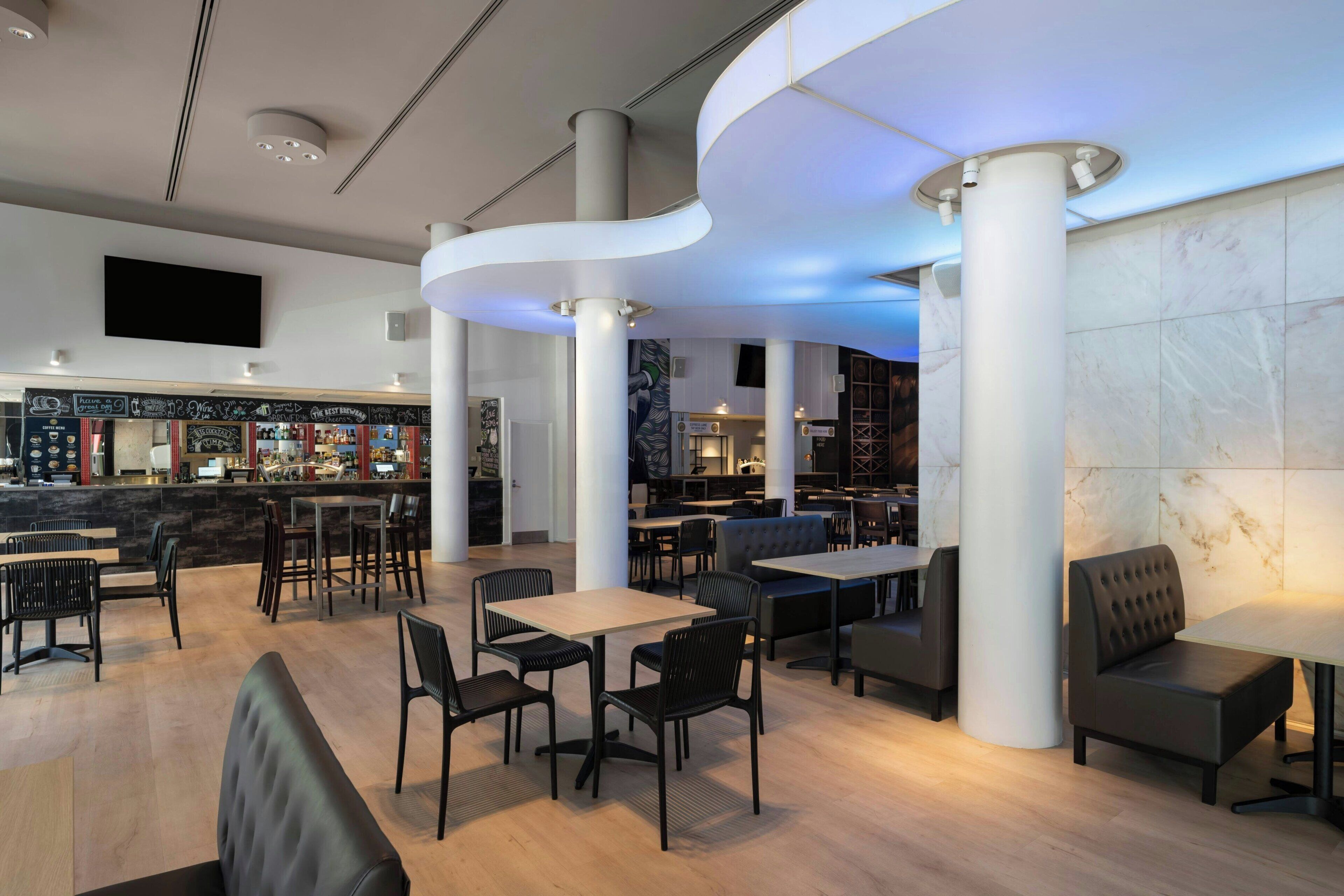 En moderne restaurant med høje lofter, et barområde og forskellige siddepladser, herunder borde og båse.