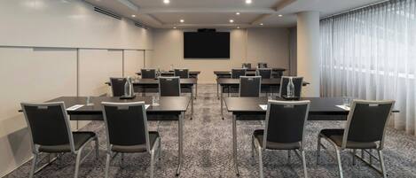 A conference room with tables, chairs, a projector screen, and a large window with curtains.
