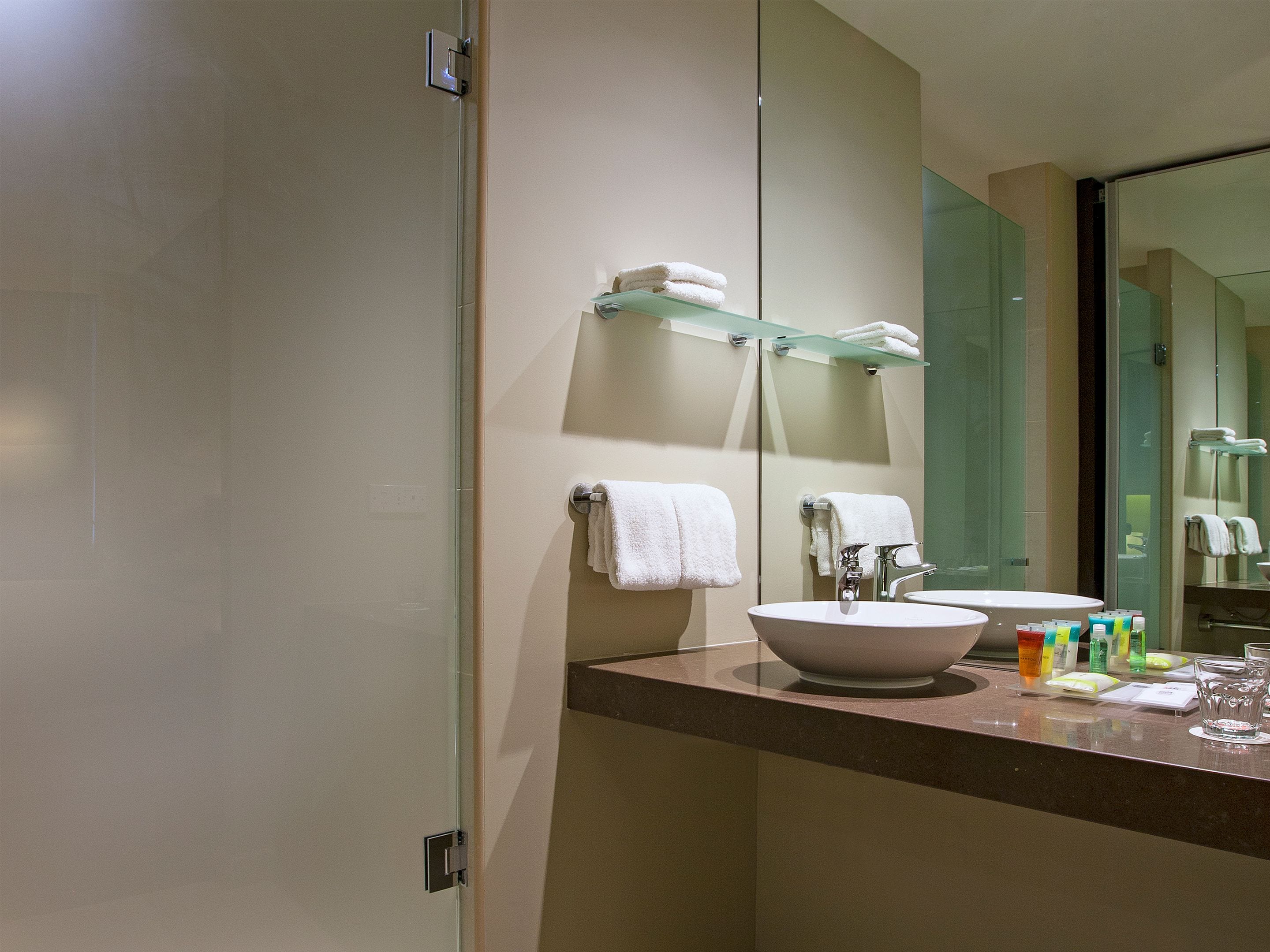 Un baño moderno con un espejo grande, un lavabo y un estante de vidrio con toallas.