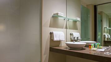 Un baño moderno con un espejo grande, un lavabo y un estante de vidrio con toallas.