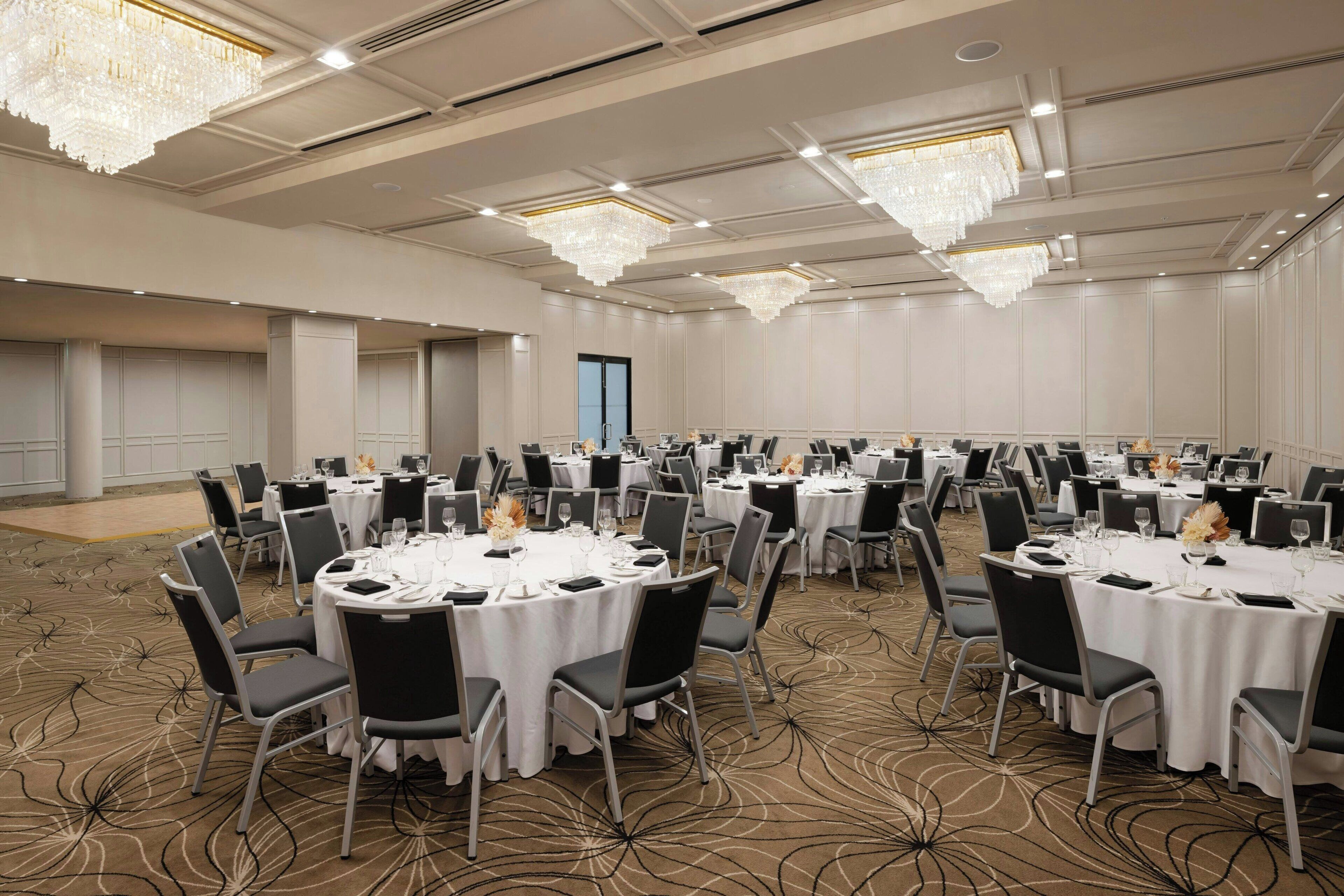 Un salón de conferencias amplio con varias mesas redondas, cada una dispuesta con sillas y manteles blancos.
