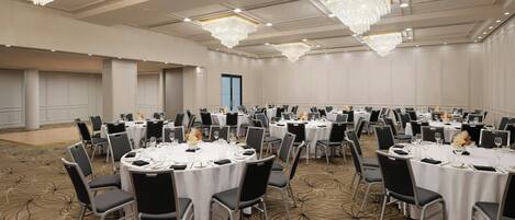 A large conference room with multiple round tables, each set with chairs and white tablecloths.