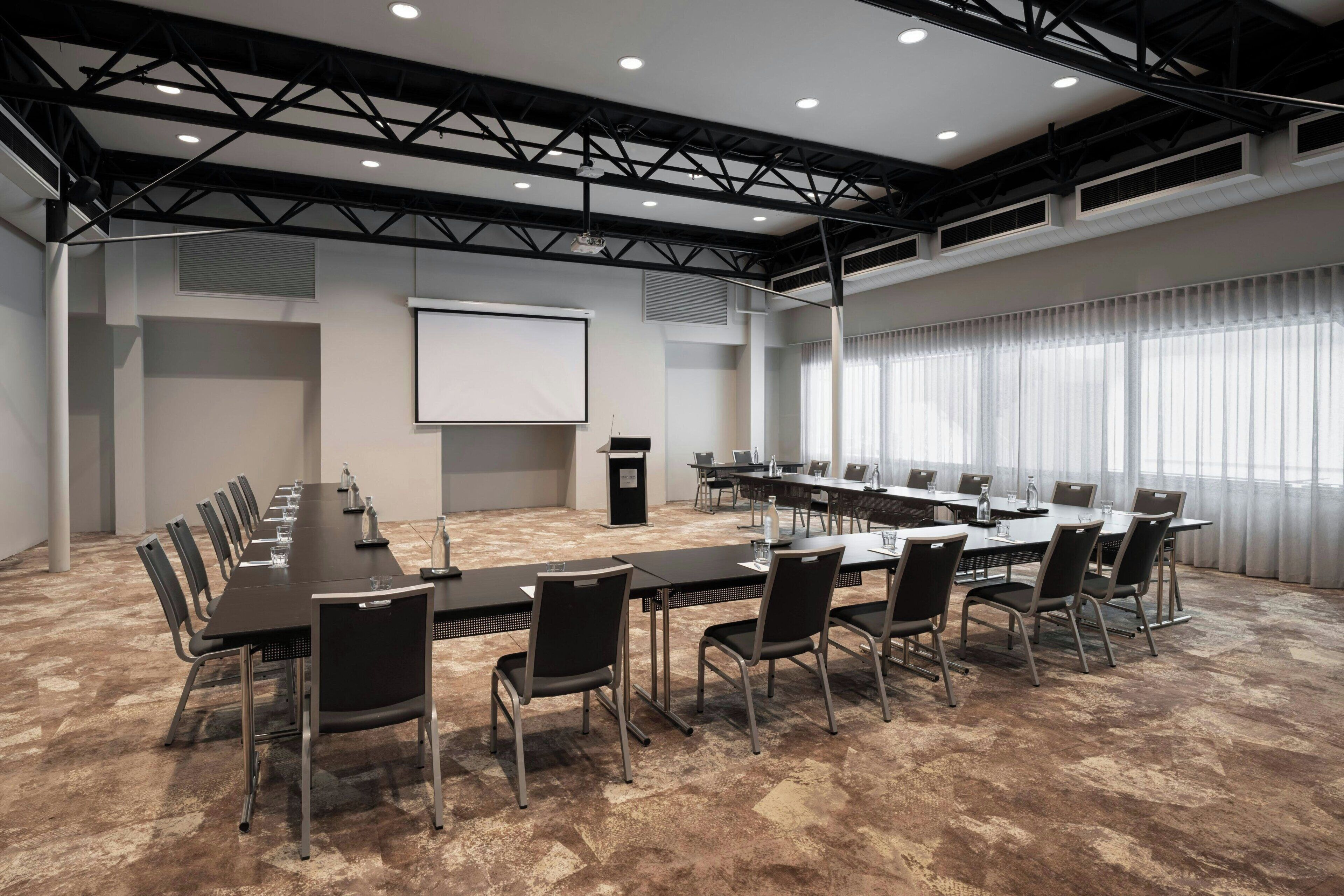 Una sala de conferencias con una larga mesa, sillas, una pantalla de proyector y un atril.
