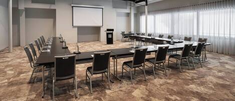 Una sala de conferencias con una larga mesa, sillas, una pantalla de proyector y un atril.