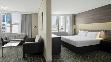 A hotel room with a bed, a sofa, a coffee table, and a view of tall buildings.