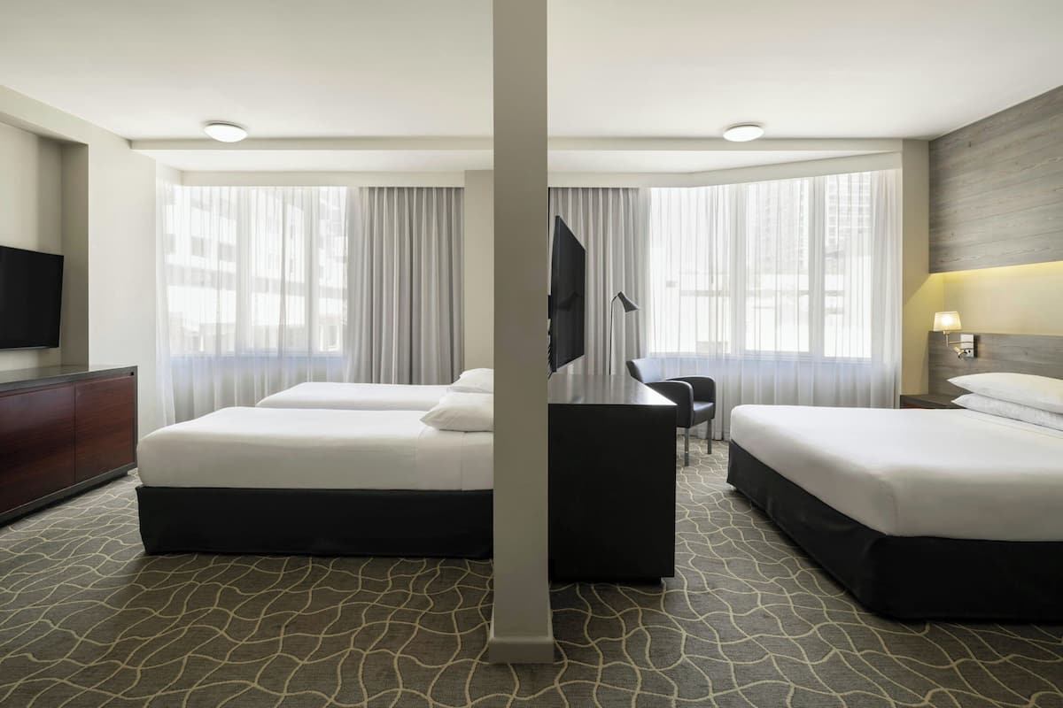 A hotel room with two beds, a flat-screen TV, a desk, and a large window with curtains.