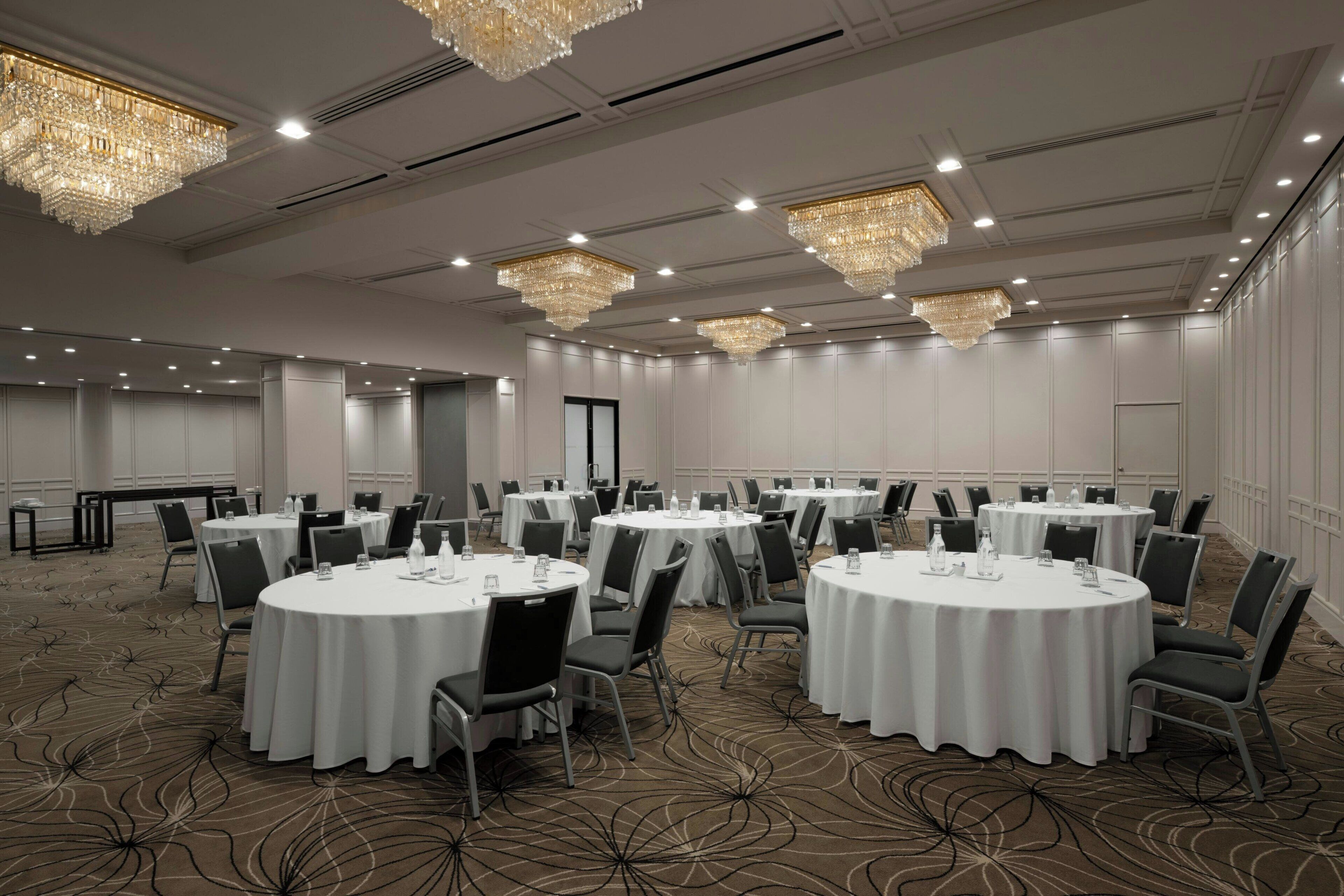 Un salón de conferencias con mesas redondas, sillas y candelabros.