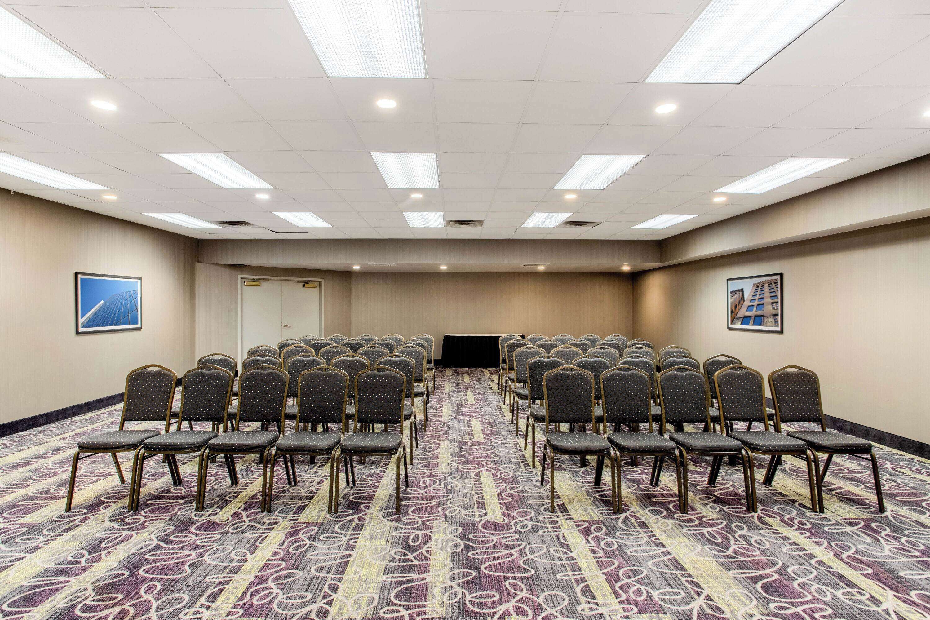 Un salón de conferencias con filas de sillas, piso alfombrado e iluminación en el techo.