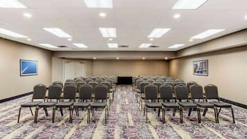 Un salón de conferencias con filas de sillas, piso alfombrado e iluminación en el techo.