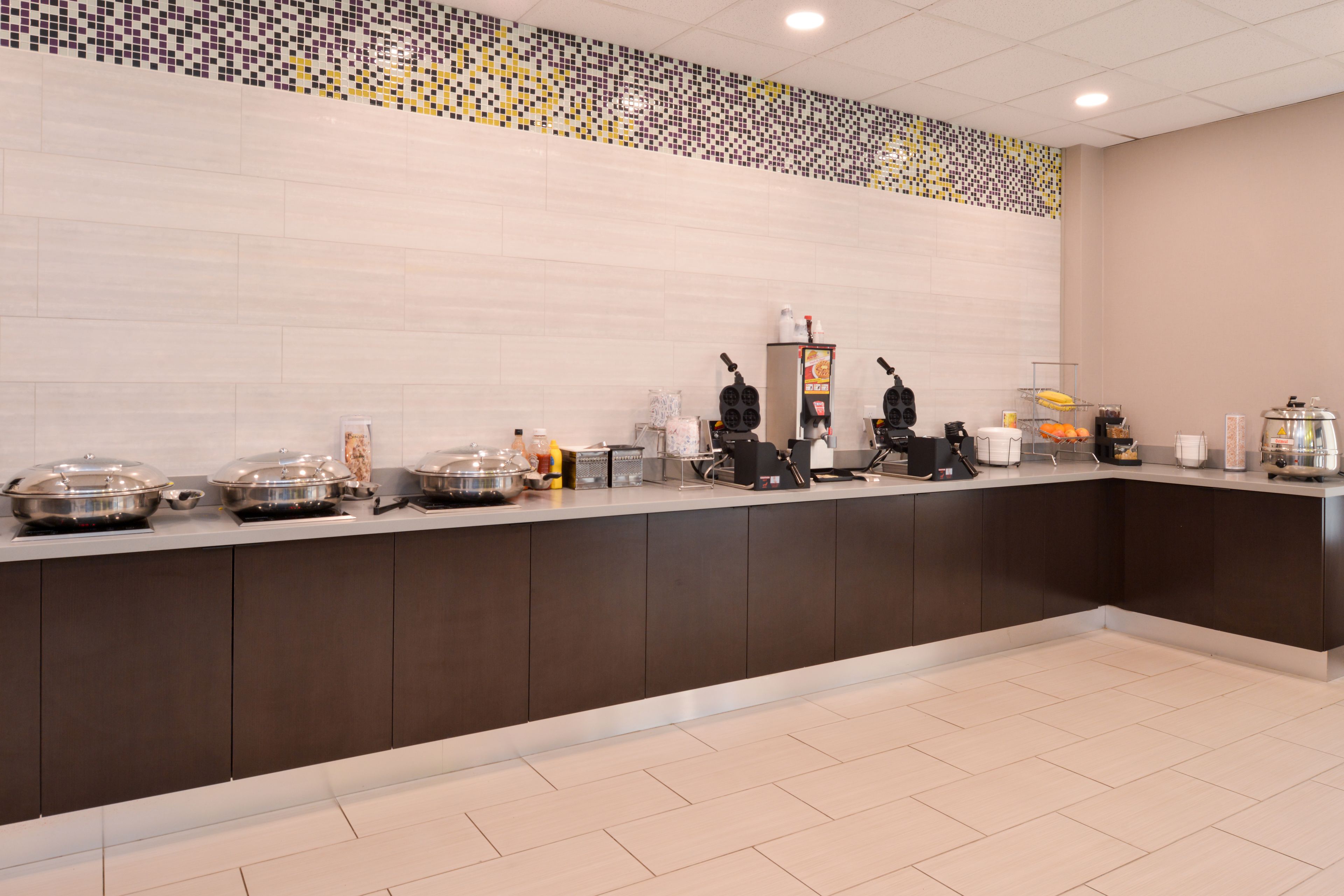 A modern breakfast bar with a tiled backsplash, self-service food stations, and a coffee machine.